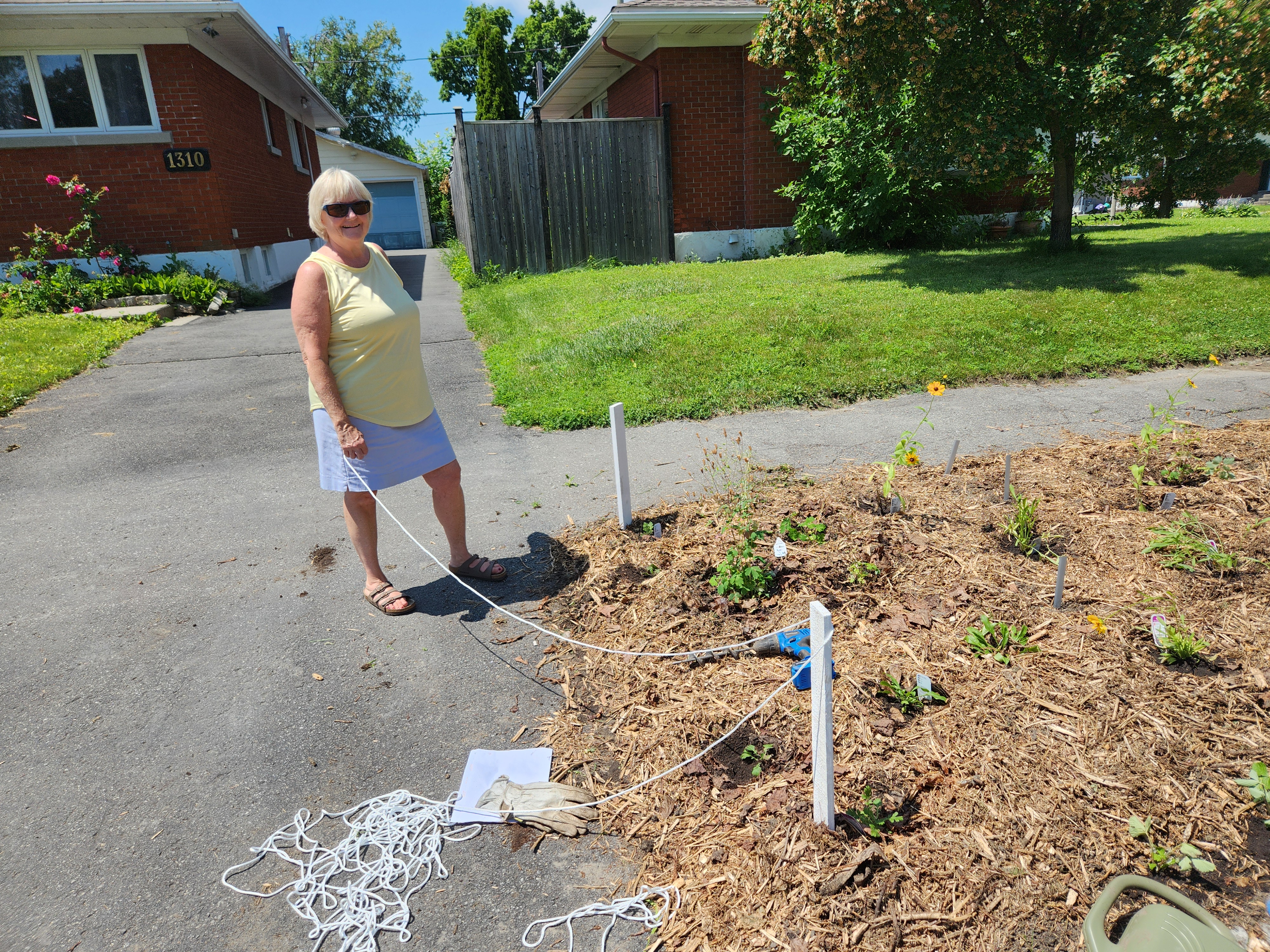 Andrea smiling while putting up a small rope fence around the Agincourt Boulevard Garden