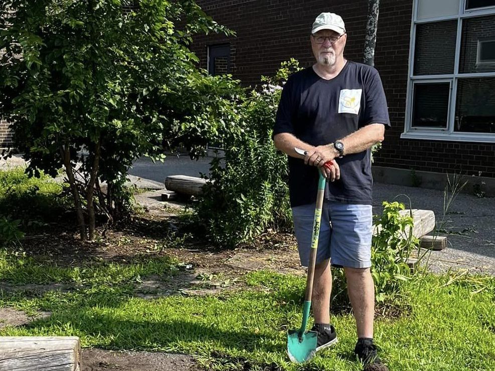 Harry standing at Agincourt School with a shovel. The ground has been turned over and grass removed. 